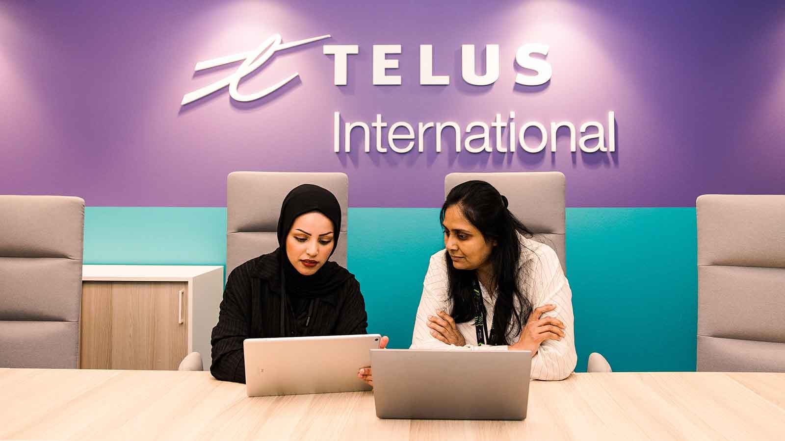 Two women sitting at a desk looking at laptops.