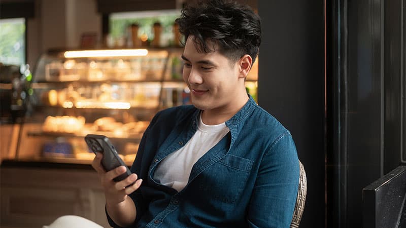 Man sitting in a coffee shop looking at his mobile device.