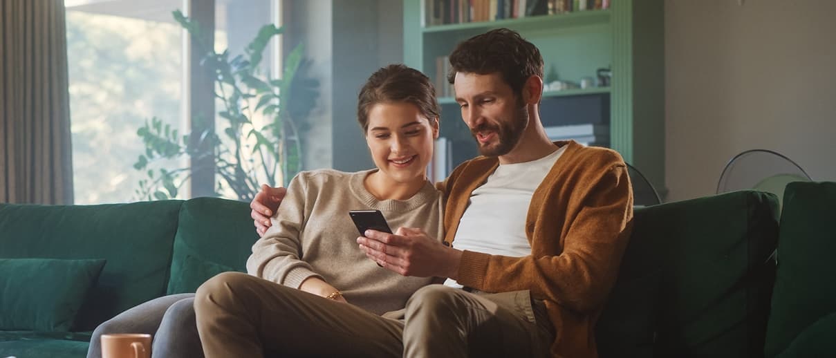 Photo of two people sitting together and looking at a single smartphone, meant to symbolize the end-users who benefit from TELUS Digital’s work acting according to humanity-in-the-loop principles.