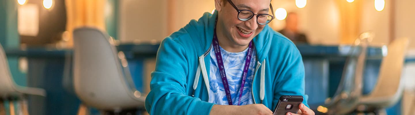 A man in a brightly lit room smiling while on his phone