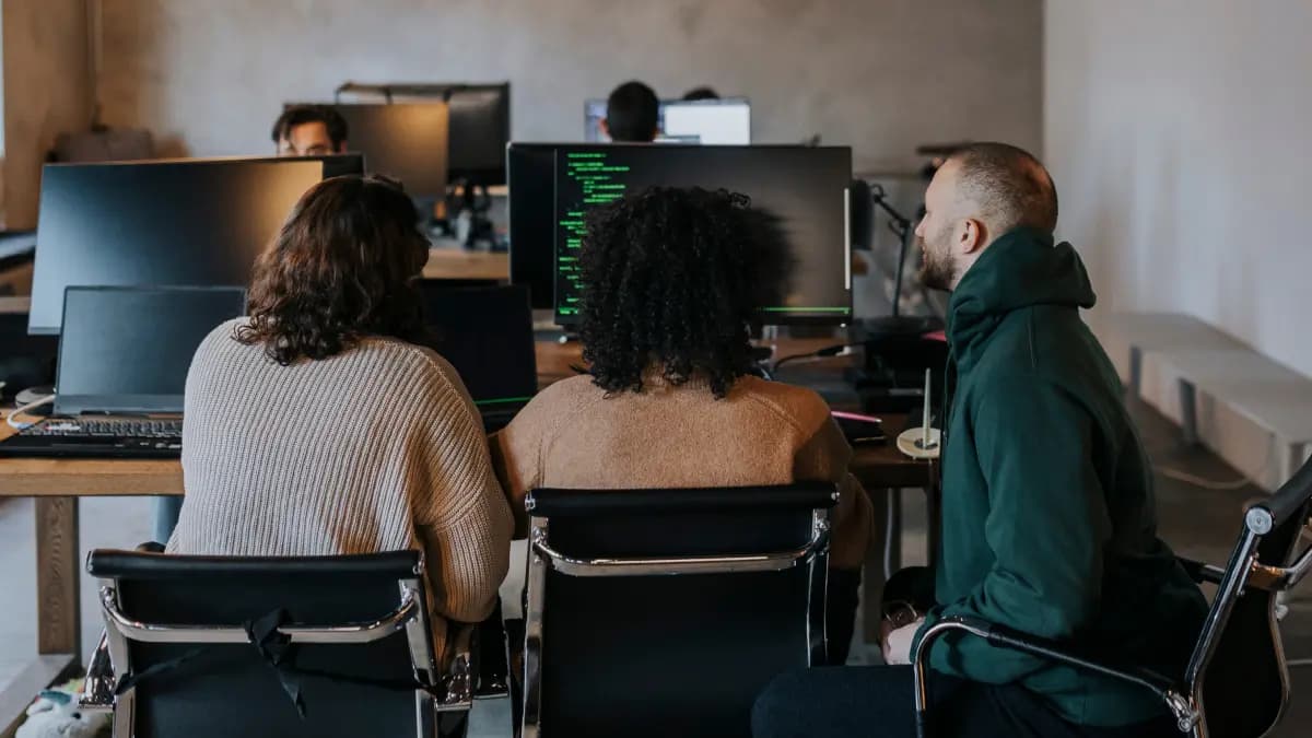 Three colleagues sitting at a desk looking at a monitor.