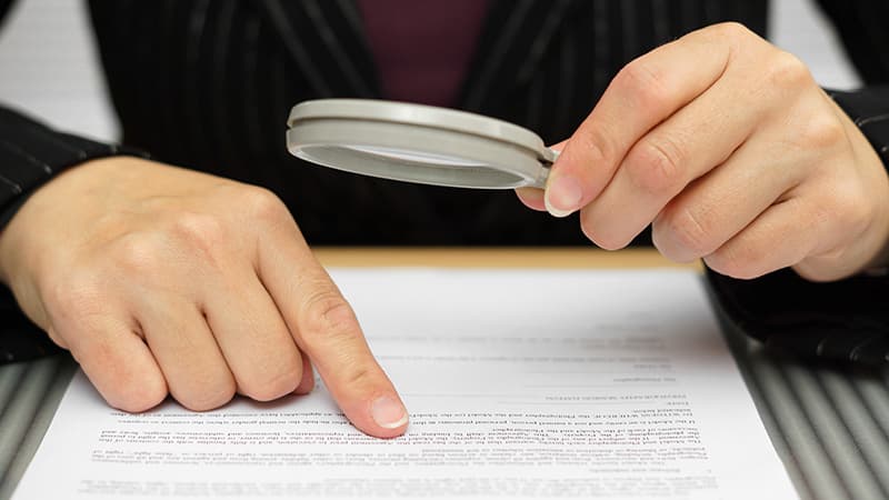 A person reviews text printed on a page using a magnifying glass.