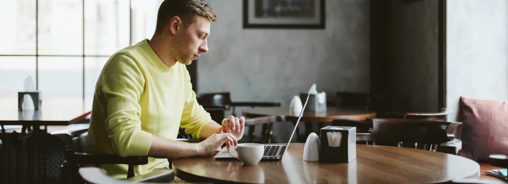 Man wearing yellow sweatshirt sitting at table using laptop