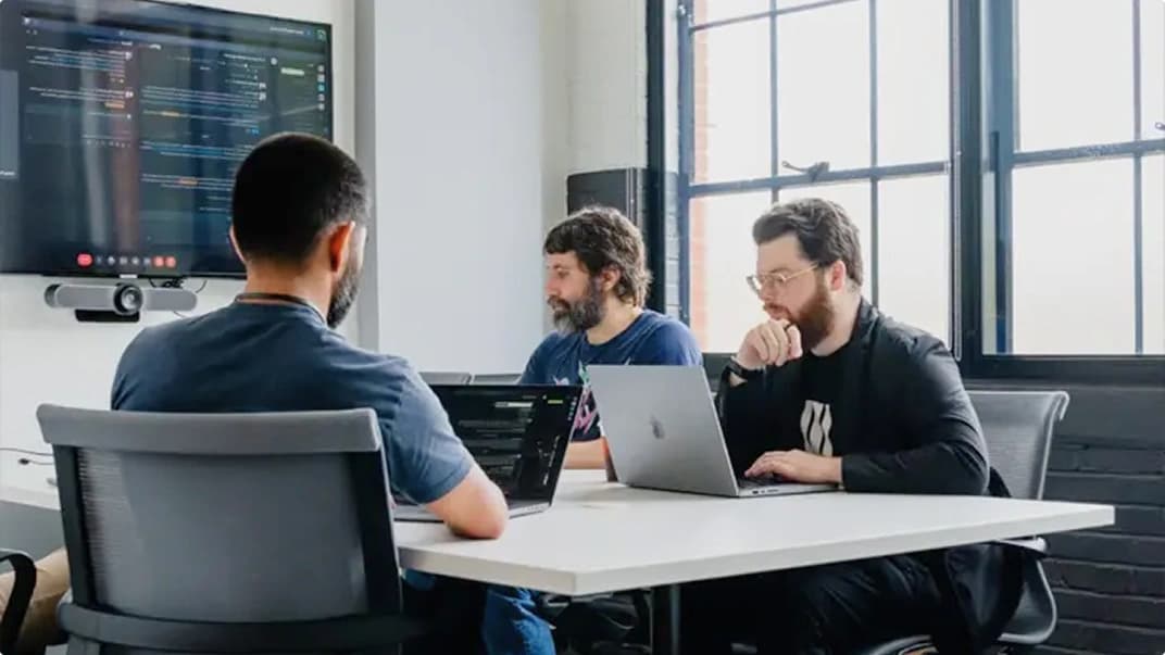 A group of people in a meeting on laptops viewing a code presentation.