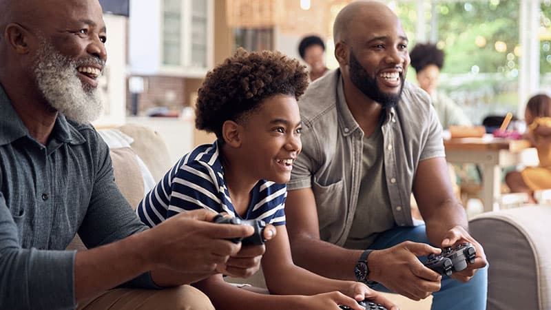 A boy (center) play video games with his grandfather (left) and father (right).