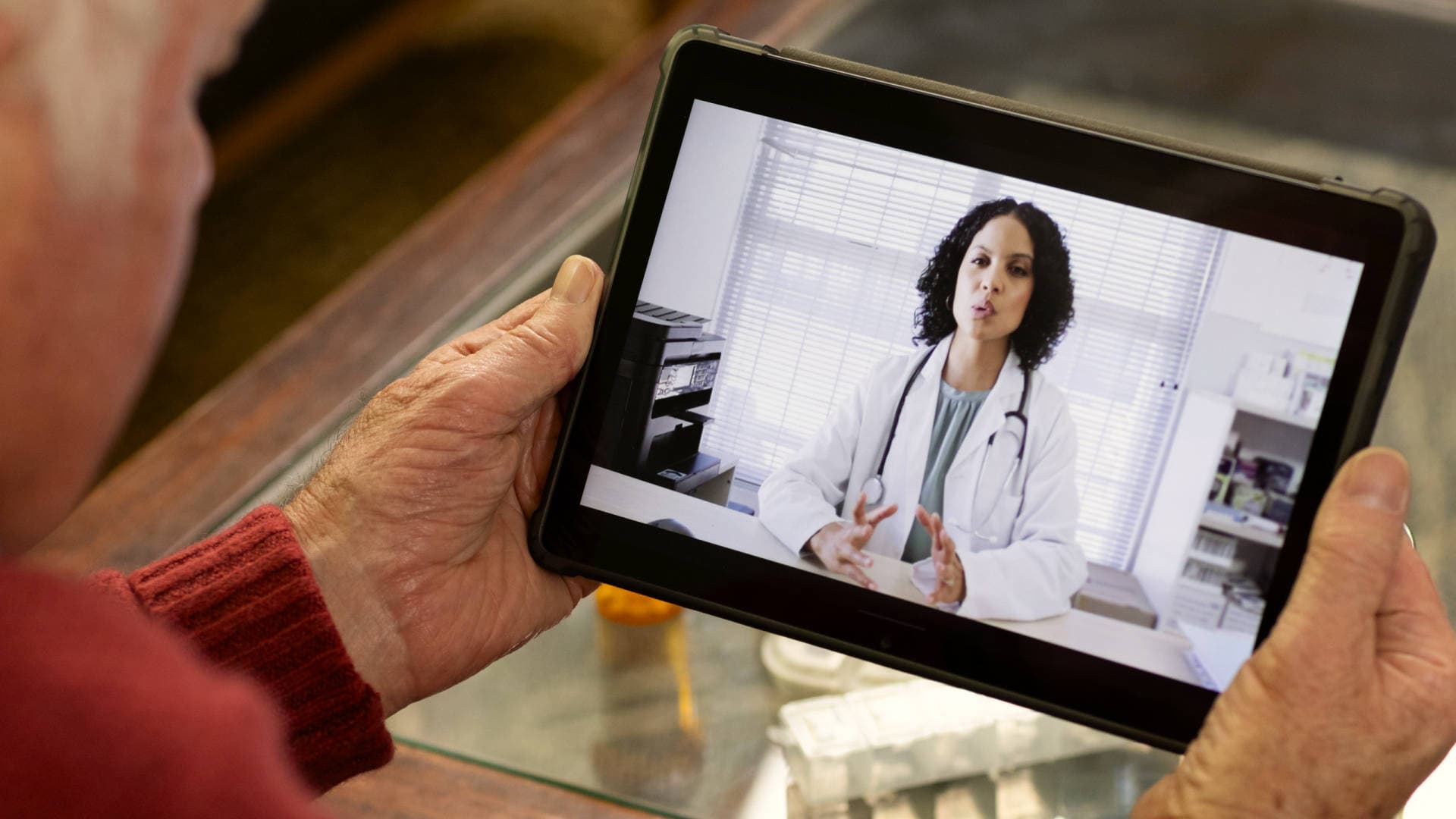 Elderly person holding a tablet watching someone in a medical coat speak.