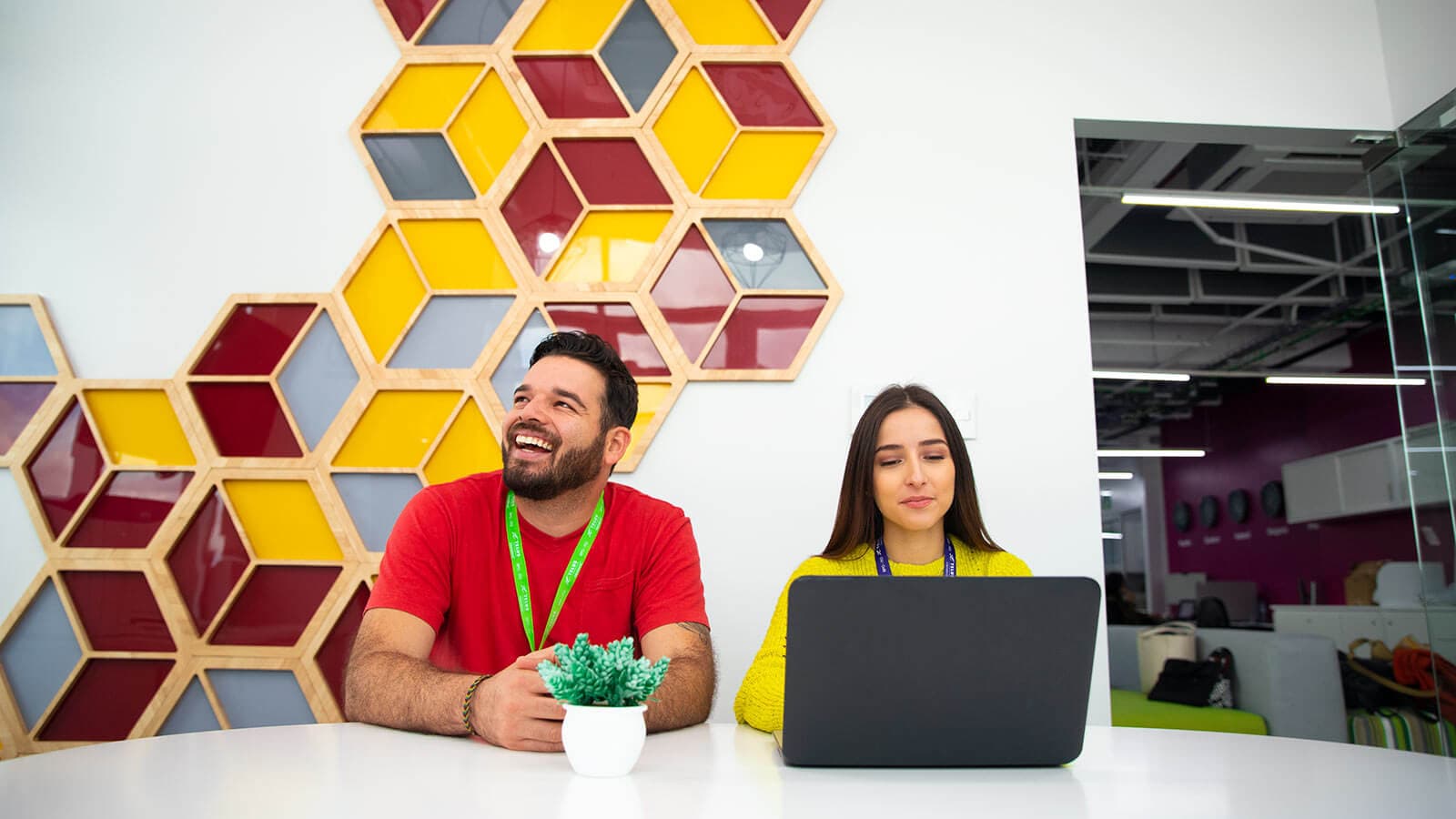 A man smiling and a woman on her laptop sitting around a table